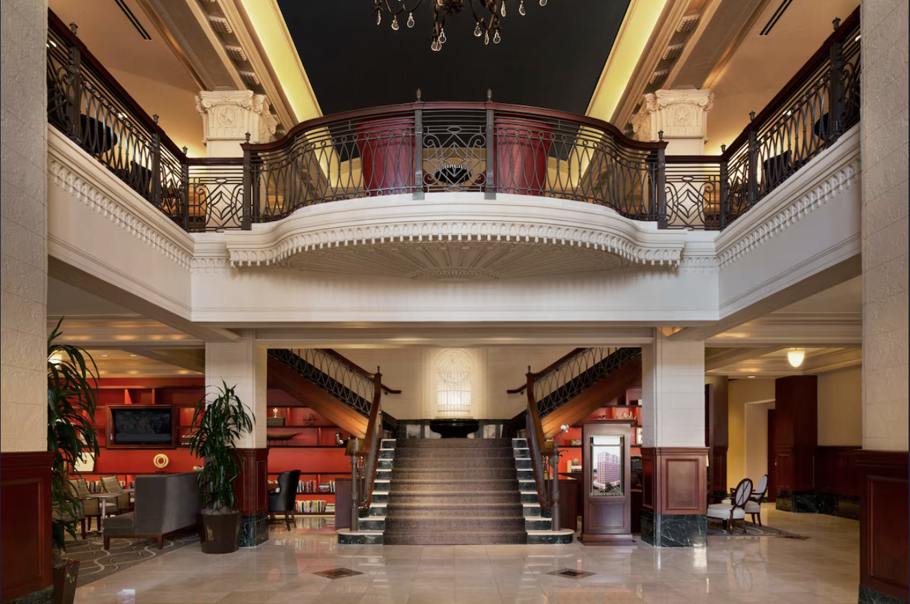 Elegant hotel lobby with grand staircase, ornate railings, and warm lighting.